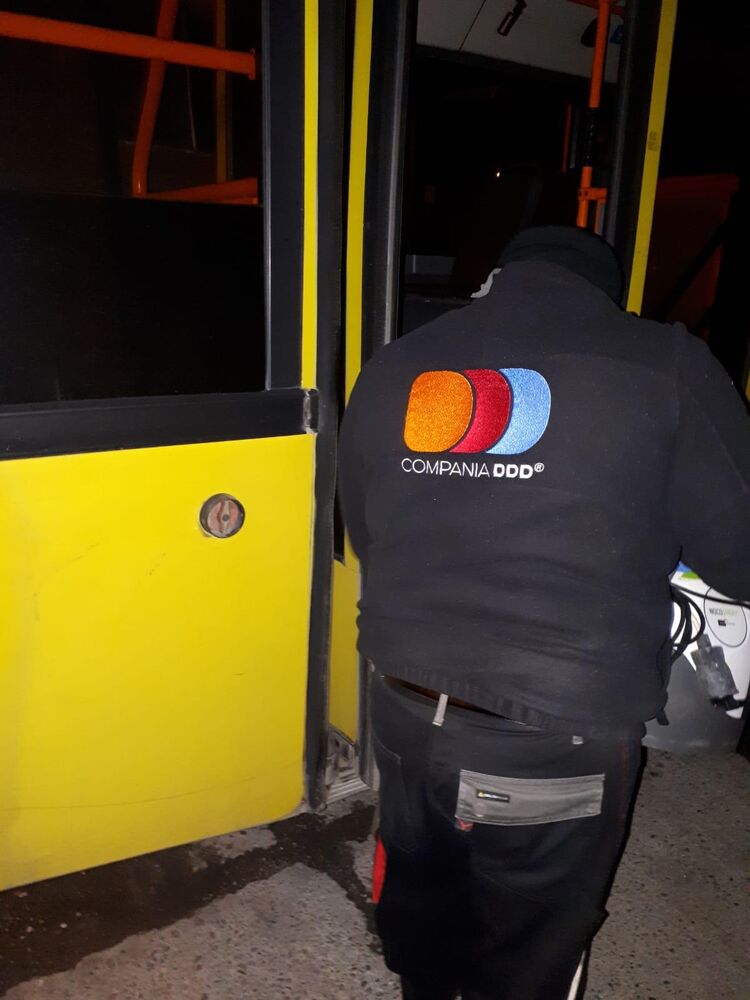 Operator Compania DDD, cu sigla firmei pe spate, urcând în autobuz cu aparatul de nebulizare