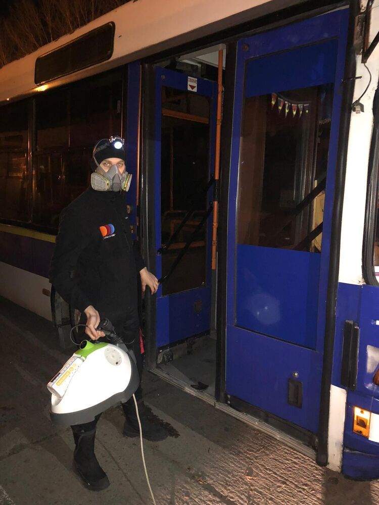 Operator în echipament complet de protecție, cu aparatul în mână, înainte de a intra în autobuz